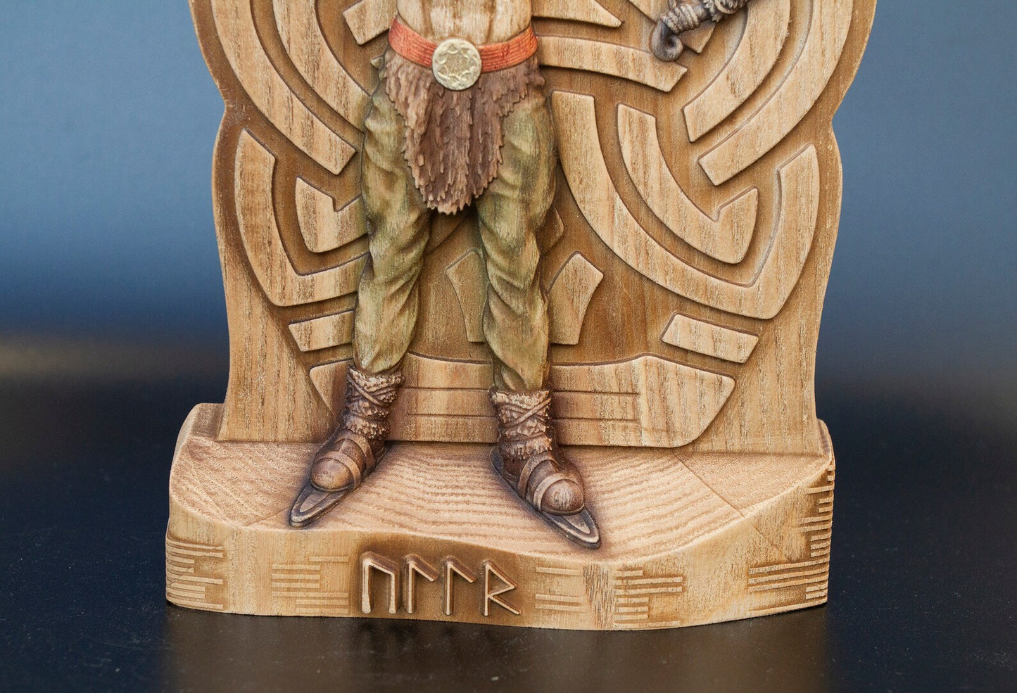 Bottom half of wooden Ullr figurine showing green pants, Viking boots on skis, and carved runes on statue base.