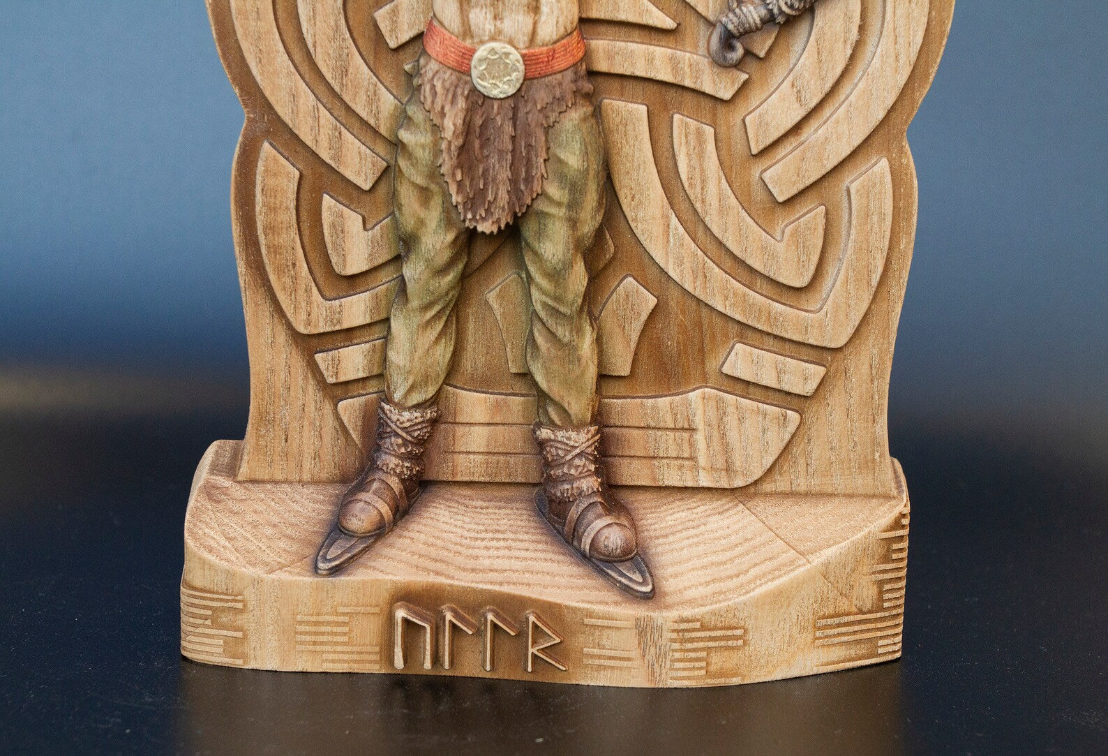 Bottom half of wooden Ullr figurine showing green pants, Viking boots on skis, and carved runes on statue base.